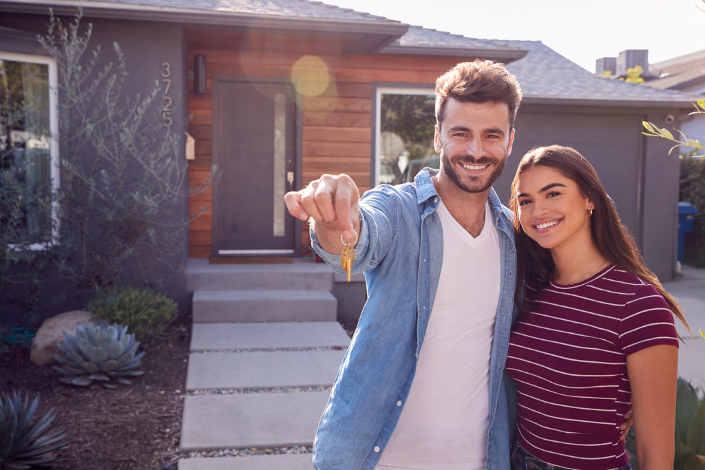 Portrait Of Homeowners Standing Outdoors In Front Of House Holding Keys