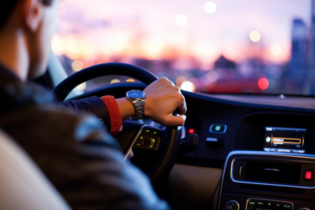 View of a Man with Great Rates from Ovation Driving a Car Towards a Sunset